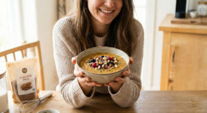 A woman holding a warm bowl of vegan keto porridge topped with fresh berries nuts and seeds in a bright kitchen